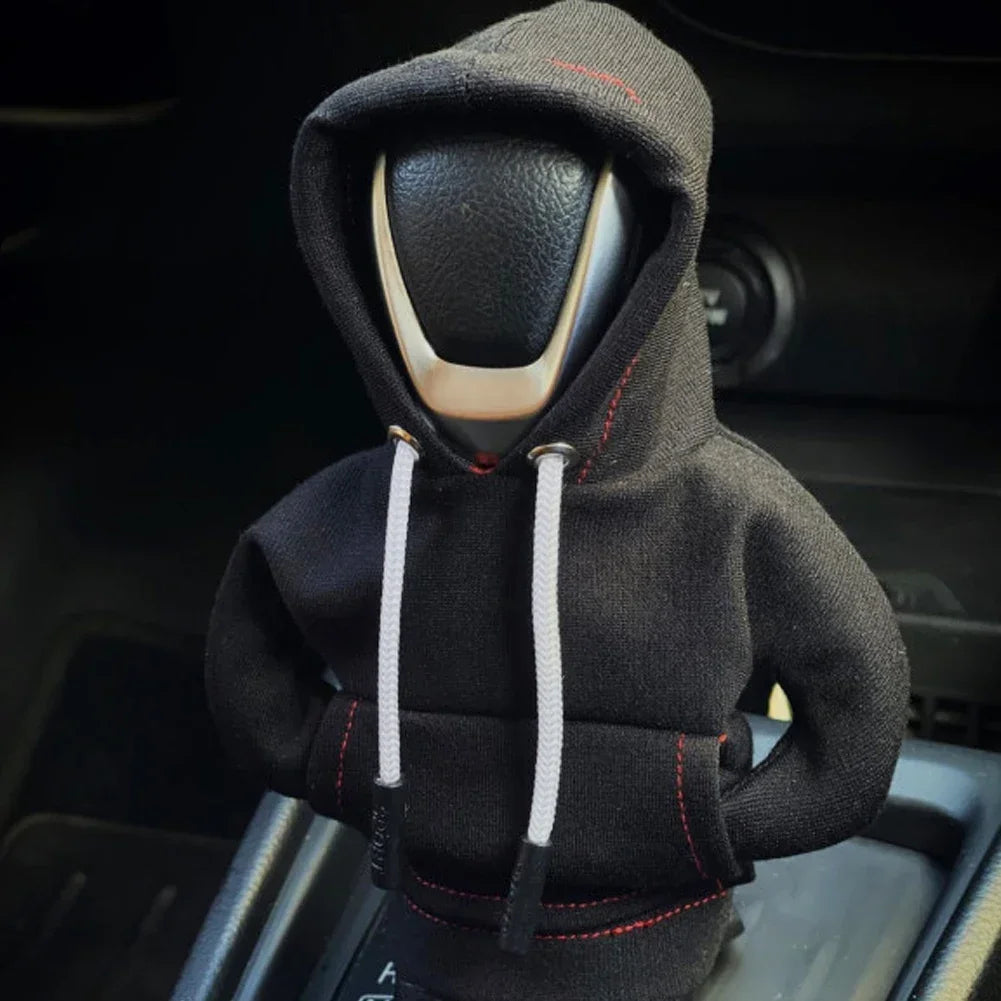 Car gear shift knob wearing a black hoodie with red stitching inside a vehicle.