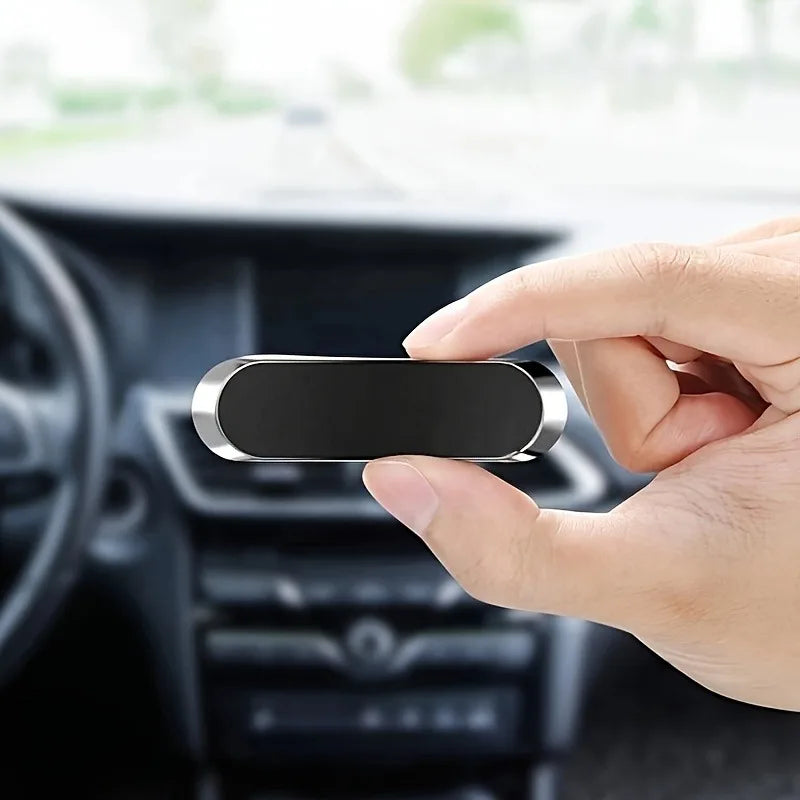 Hand holding a black and silver car air freshener against a blurred car interior background