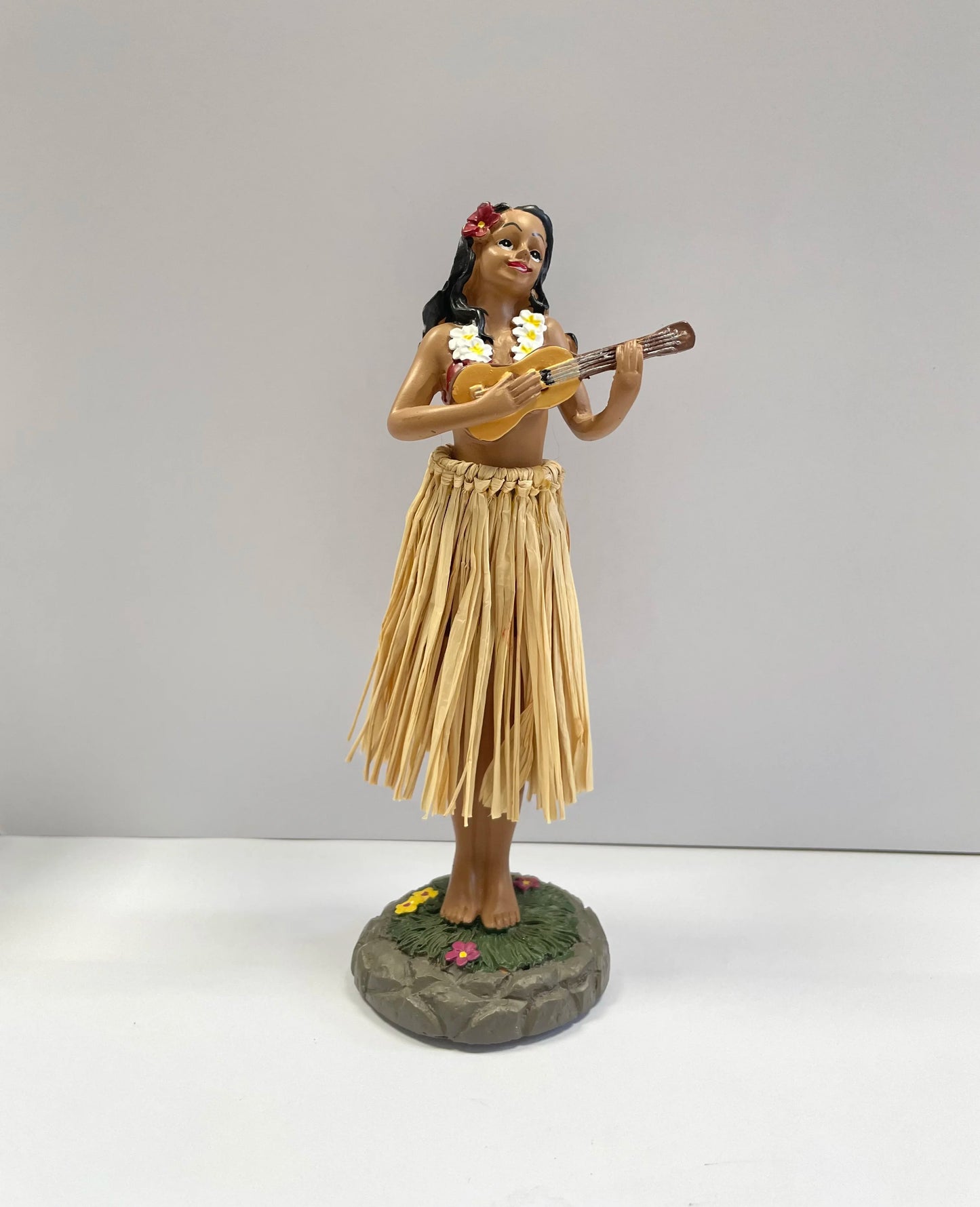 Statue of a hula dancer playing a ukulele on a white background