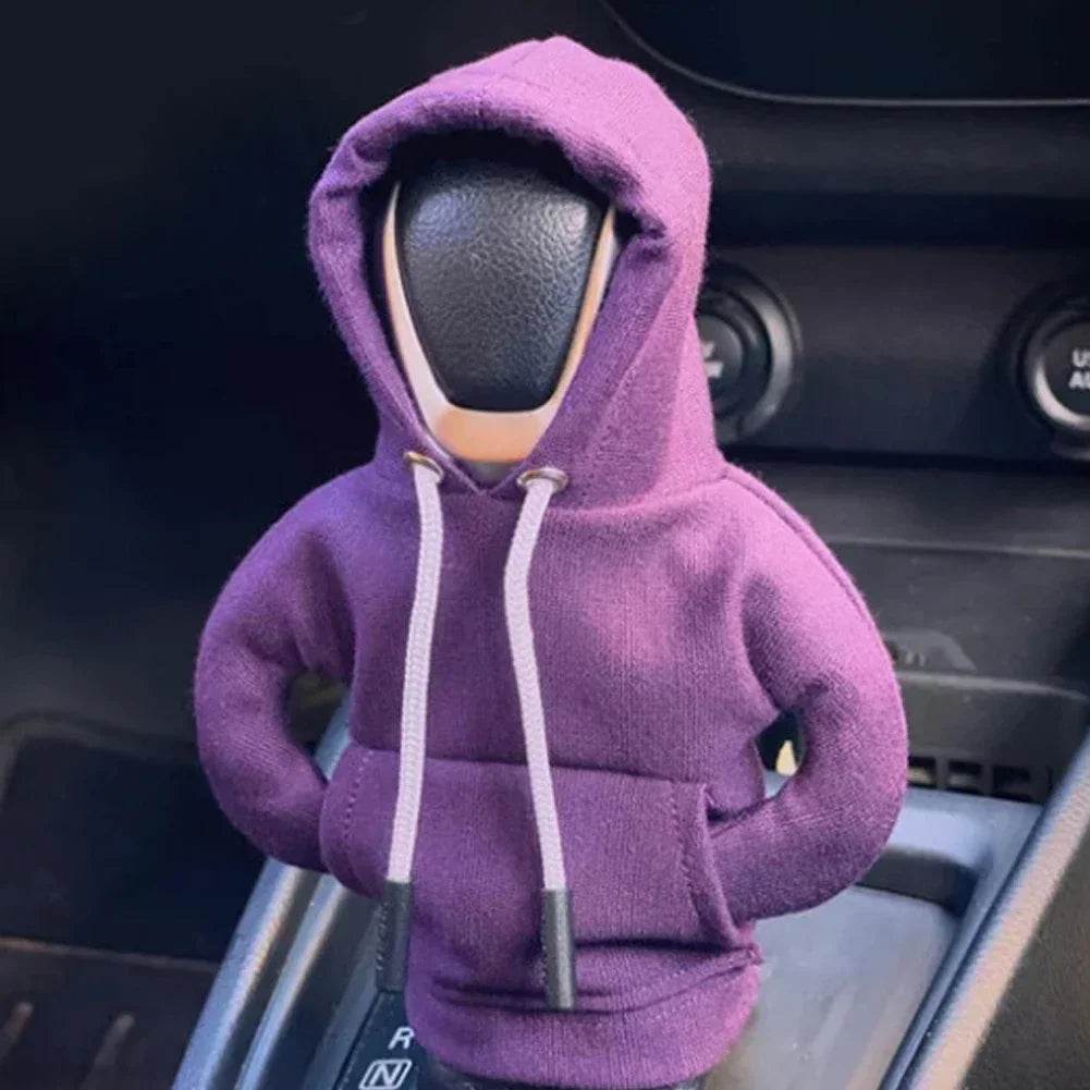 Toy figure wearing a purple hoodie inside a car.