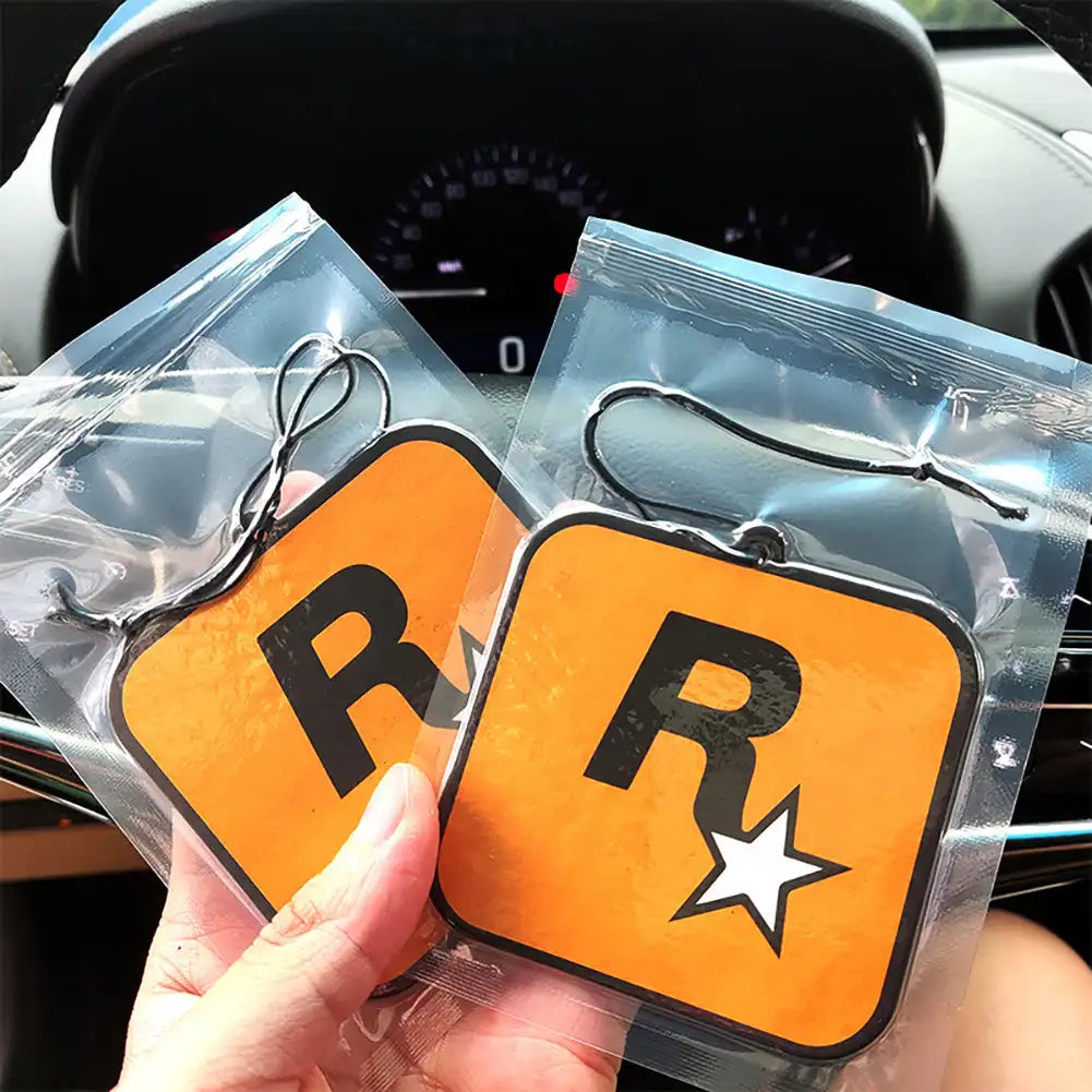Two orange car air freshener tags with 'R' and star design held in front of a car interior.
