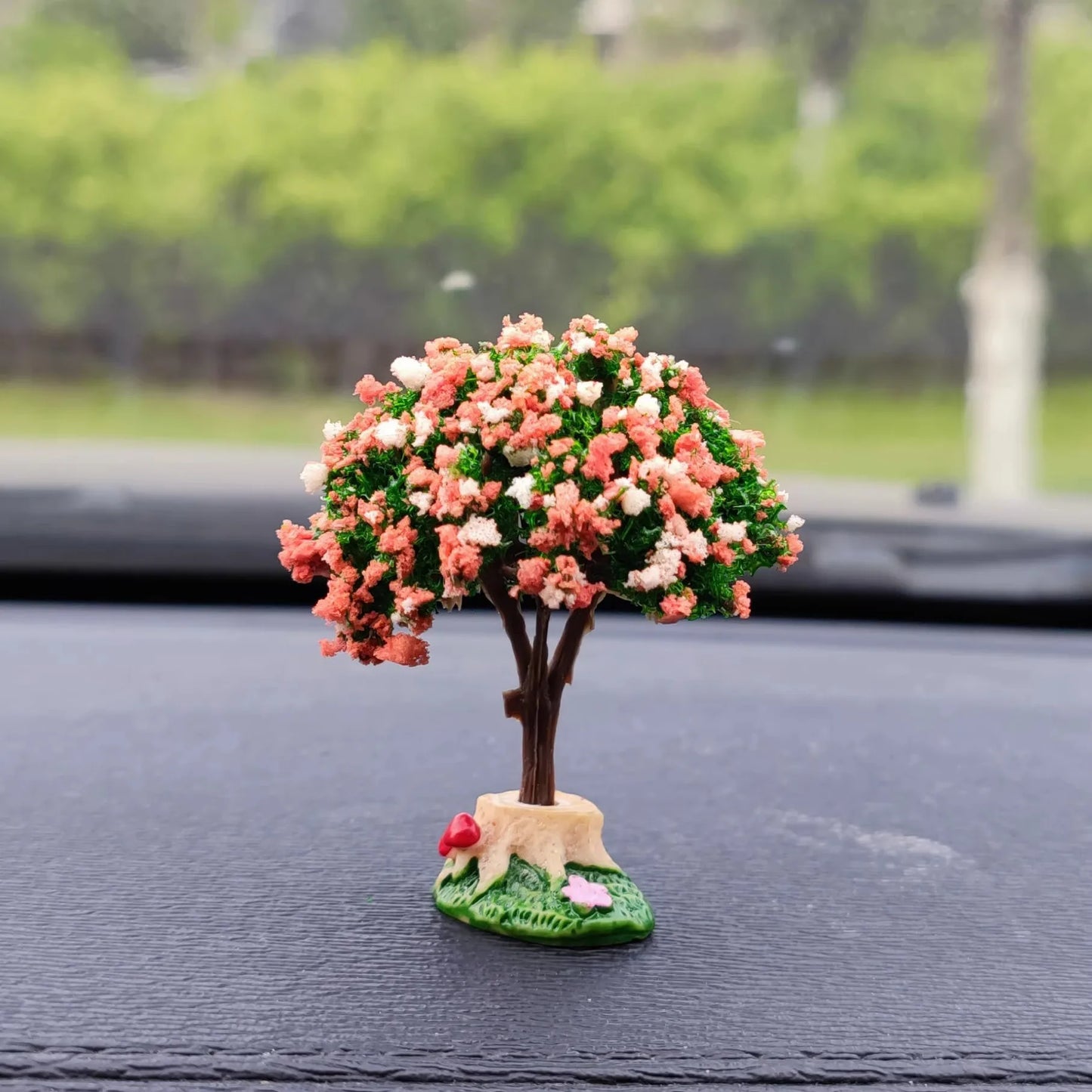 Decorative tree figurine with pink flowers on a car dashboard.