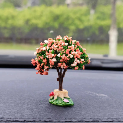 Decorative tree figurine with pink flowers on a car dashboard.
