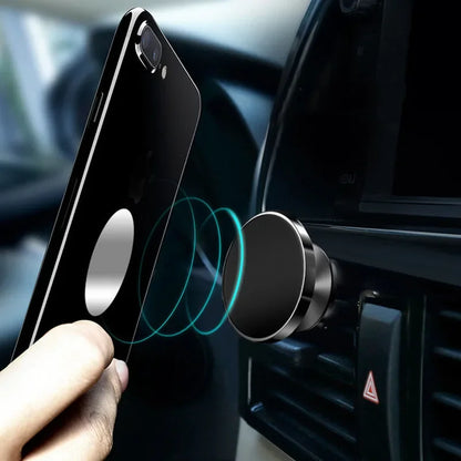 Hand holding a phone above a magnetic car mount in a vehicle.