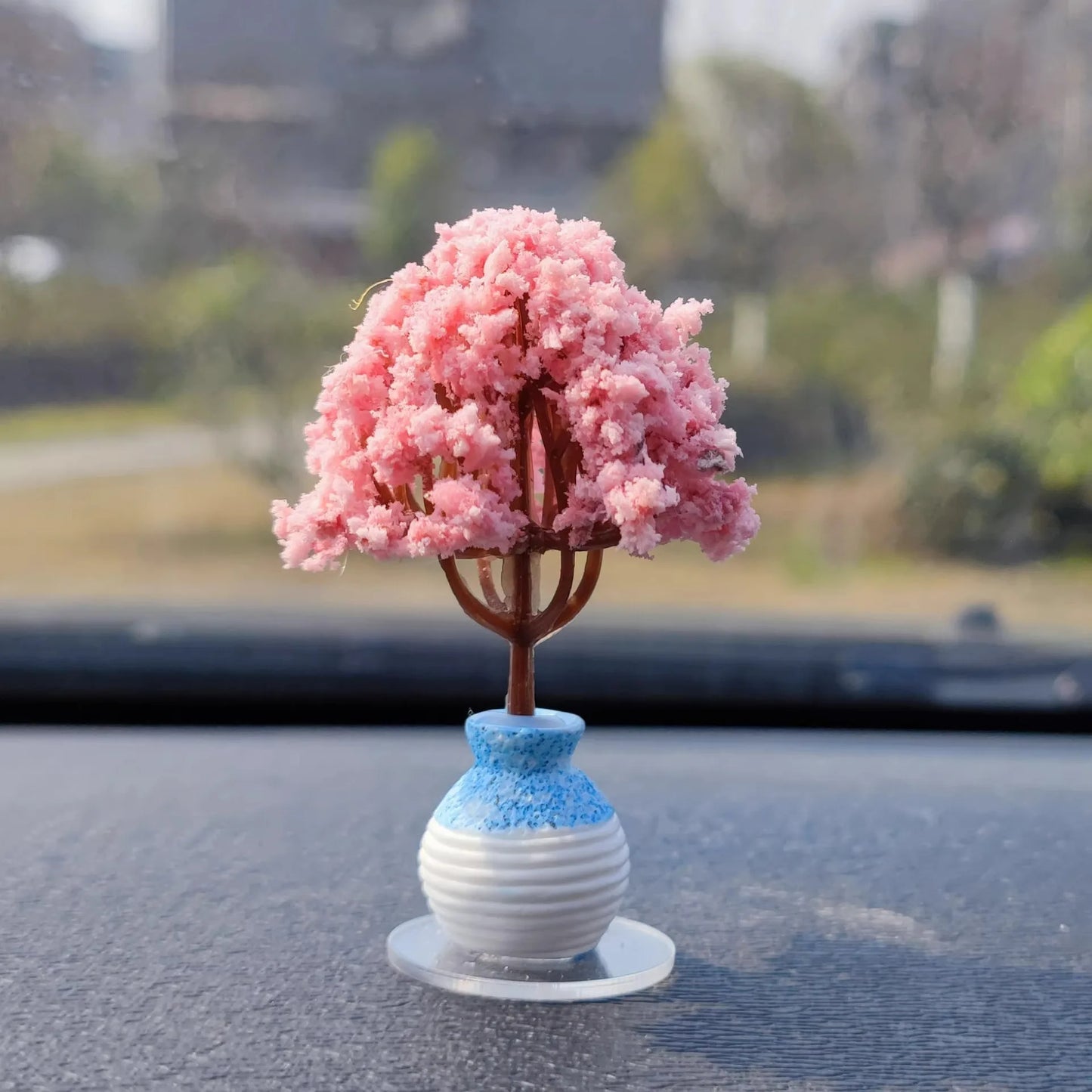 Model of a pink flowering tree on a blue and white base with a blurred outdoor background