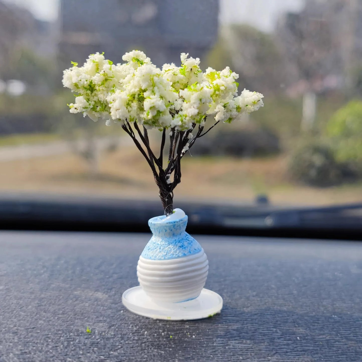 Small white floral arrangement in a blue and white vase on a reflective surface with a blurred outdoor background